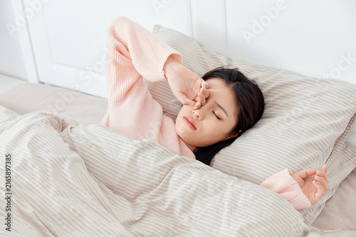 Bild auf Leinwand Young girl waking up in bed at home in bright bedroom