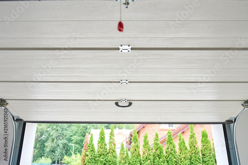 Sectional garage door is partially open with a view outside from inside the garage