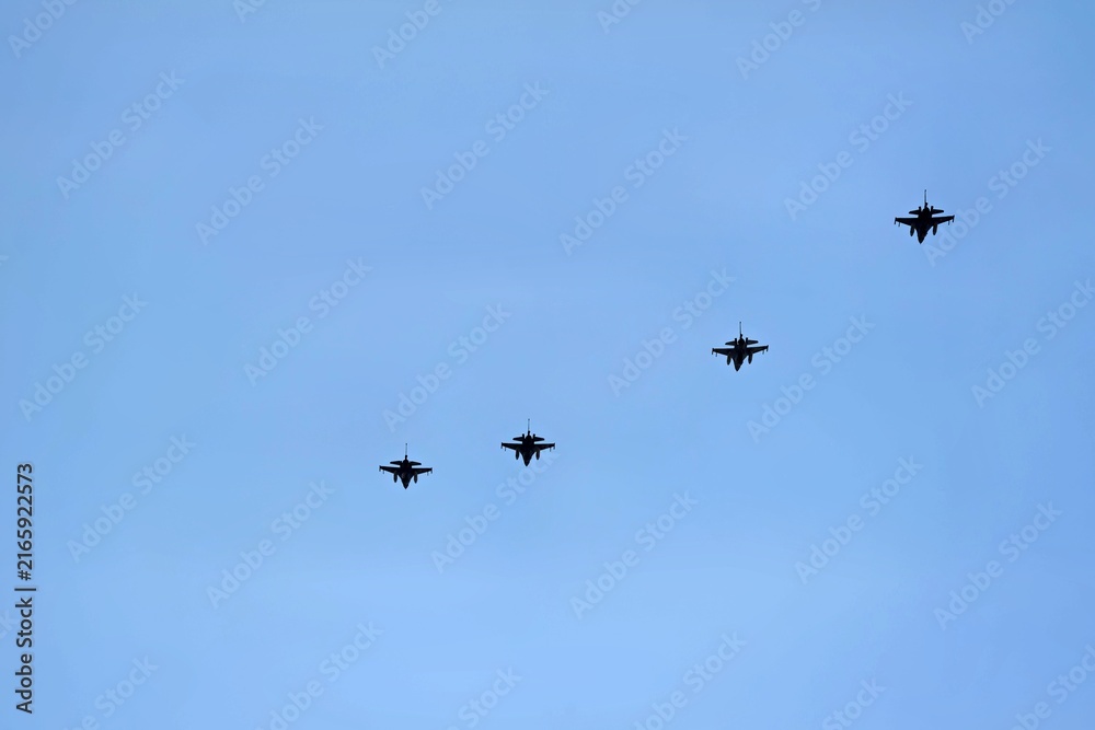 Fototapeta premium A formation of four fighter jets flying across a clear blue sky. The sleek aircraft are seen in a straight line, showcasing their design and military capability.