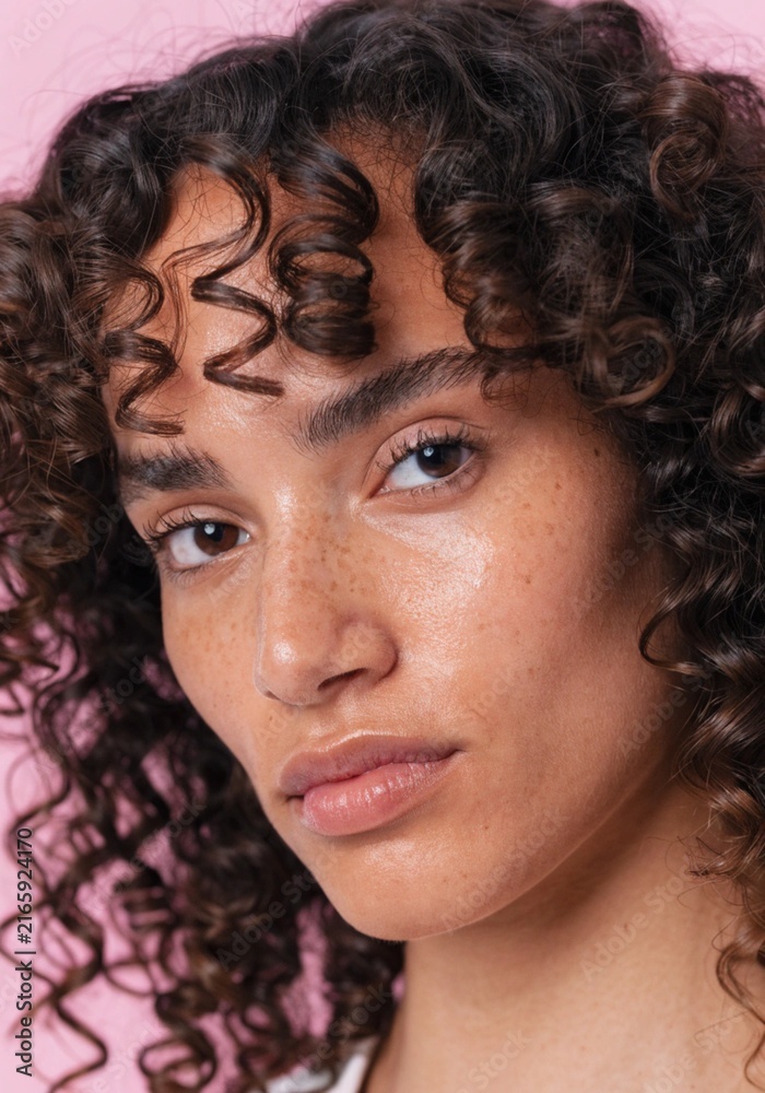 Fototapeta premium Portrait of Woman with Curly Hair Against Soft Pink Background