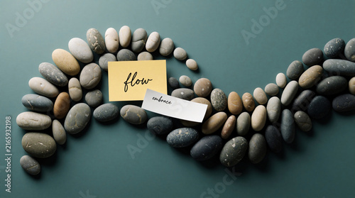Smooth river stones form a wave pattern with sticky notes saying flow and embrace. Concept symbolizes acceptance, progress, and natural transition.