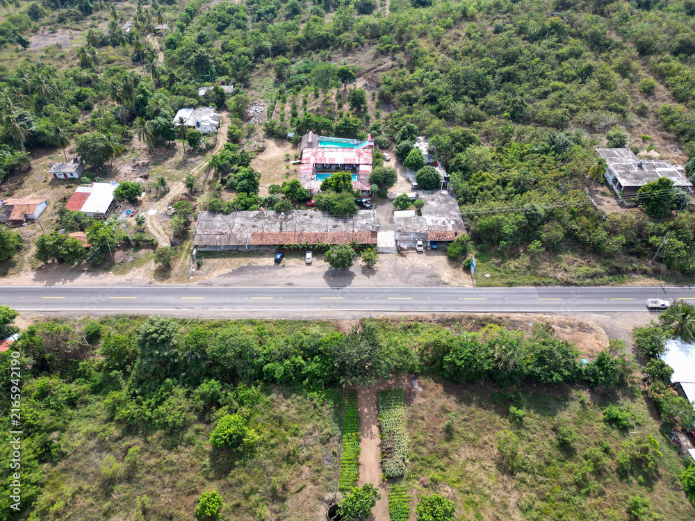 Fototapeta premium Aerial drone view shows vibrant ranch with blue pool and buildings, highway, lush tropical nature in Guerrero, Mexico, sunny day