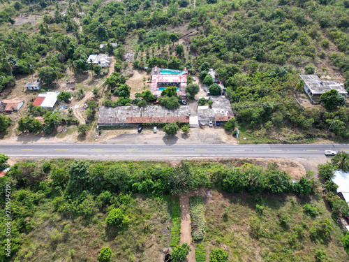 Aerial drone view shows vibrant ranch with blue pool and buildings, highway, lush tropical nature in Guerrero, Mexico, sunny day