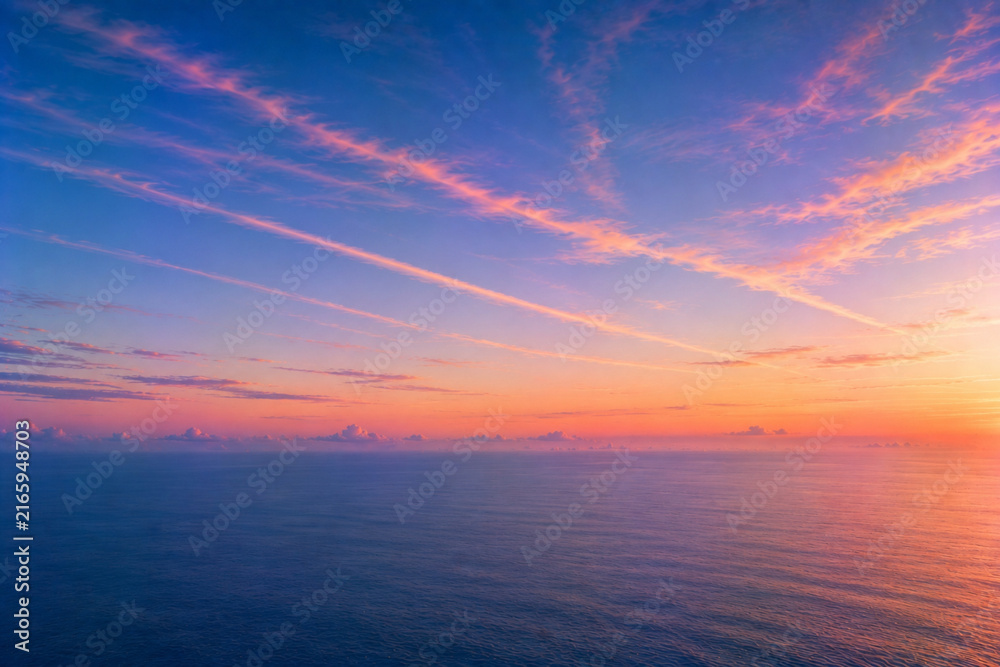 Fototapeta premium Pink sunset clouds over calm blue ocean and distant horizon