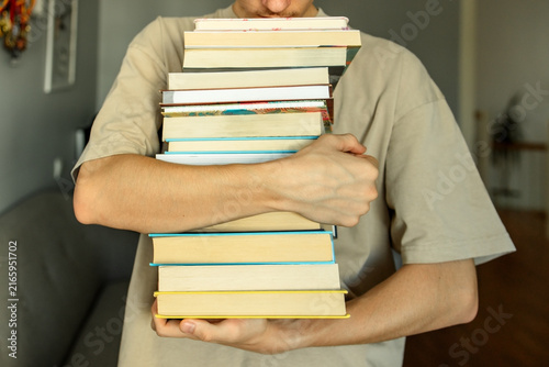 Young man holding huge heavy stack of books