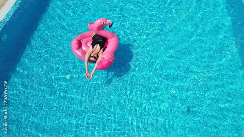 Aerial drone view of woman relaxing on flamingo pool float in pool in hotel. Summer holidays, enjoying summer vacations, luxury hotel
