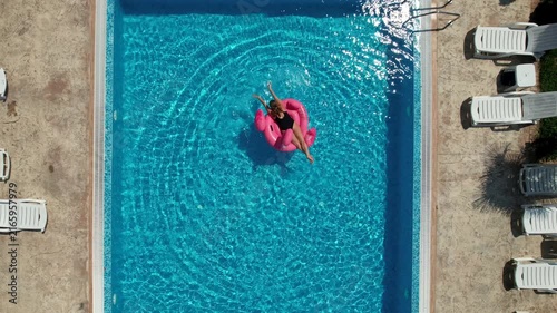 Summer holidays, relaxation. Woman on flamingo pool float in pool. Enjoying summer vacations. Aerial drone view
