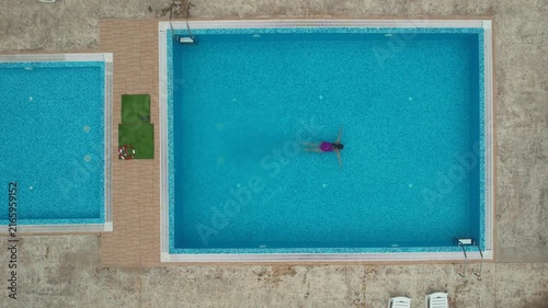Drone view from above of young woman swimming in turquoise pool water in hotel. Summer holidays, enjoying summer vacations. Aerial top view from drone. Beach vacation
