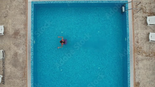 Drone view from above of young woman swimming in turquoise pool water in hotel. Summer holidays, enjoying summer vacations. Aerial top view from drone. Beach vacation
