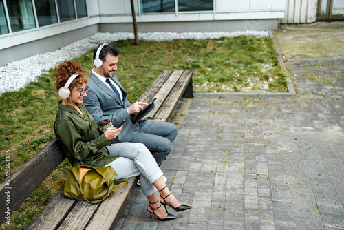 People sitting on a bench with headphones, enjoying drinks and using a tablet