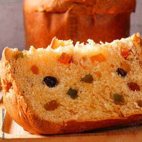 A slice of traditional Christmas panettone, showing its soft, fluffy crumb, candied fruit, and raisins, on a bamboo tray