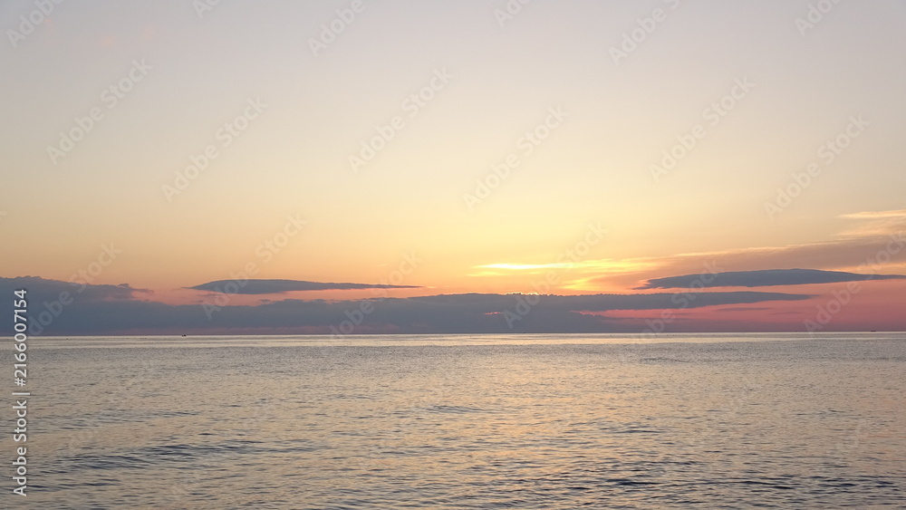 Obraz premium Sunrise over calm ocean horizon in East Sea. Scenic sunrise over the calm ocean horizon with colorful gradient sky and soft clouds in Gangneung, South Korea.