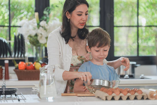 Fotografie The mother and son sift flour into a bowl while baking in a bright sunlit kitchen