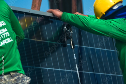 Cuadro en lienzo Thai workers in green uniforms and yellow safety helmets precisely slide modules one by one off the strapped stack in close detail high on an industrial warehouse roof in a Thai city