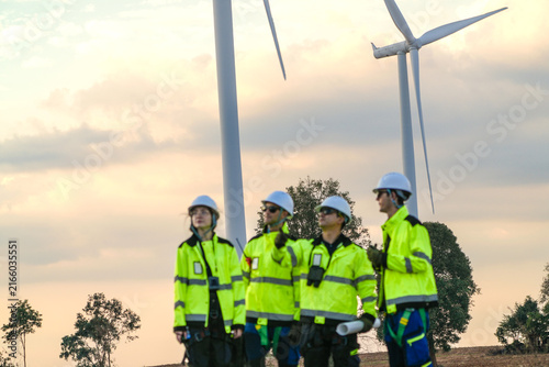 The wind farm crew of four walk abreast down the centre line at dusk on the park road under fading skies in pink pastel dusk on a working wind farm in rural Thailand.
