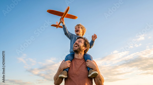 Father and Son Playing with Toy Airplane Outdoors Under a Blue Sky