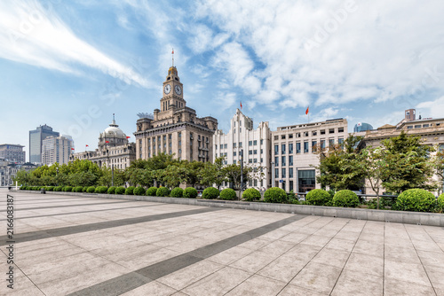 Photography A view of historic European-style buildings along Shanghai's waterfront, with a spacious paved square and greenery in the foreground under a bright sky