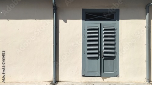 Historic colonial style grey double door with louvered shutters and a transom window on a cream building wall. Concept of vintage exterior architecture, heritage design, and urban building photography