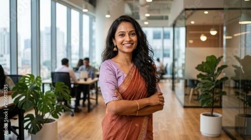 Smiling indian woman wearing traditional ethnic saree stands in contemporary office environment representing cultural pride.