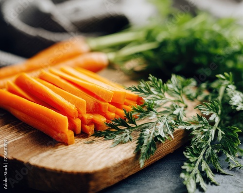 Sliced carrots on wooden board with fresh greens