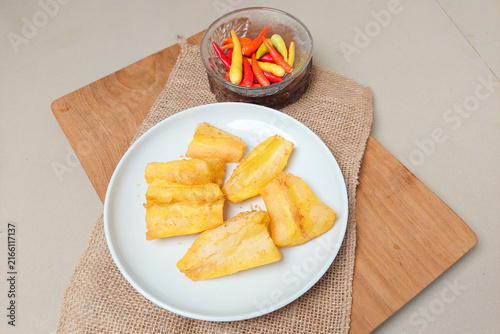 Foto Fried cassava pieces served on a white plate with red chilies and a rustic-style natural garnish, set against a wooden background