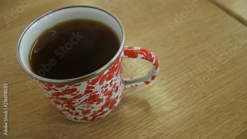 Принти на полотні A hot cup of black coffee or tea served in a traditional red and white speckled enamel mug on a light wooden table