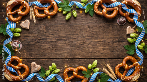 Oktoberfest background with pretzels, hops, and blue ribbon on wood