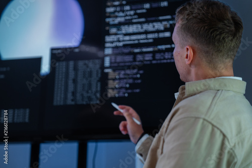 Konstfotografi A dark-haired network defence analyst extends a hand toward the glowing screen in a shadowy data monitoring room lit by screen glow, during an overnight monitoring shift