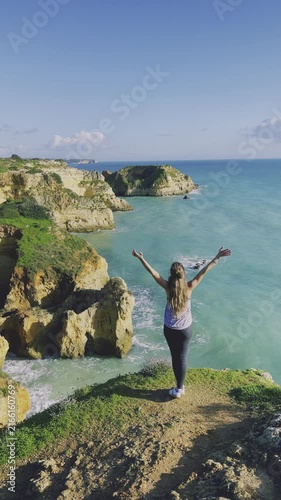 Woman with Raised Arms Standing on Cliff Overlooking Ocean, Freedom and Success Concept, Algarve, vertical footage