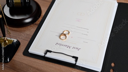 Official marriage certificate lies over wooden desk, facilitating marriage registration paperwork inside court setting, marriage license approval requiring valid certificate status beside judge gavel.