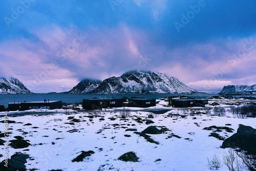 Majestic winter landscape of Lofoten islands in Norway at sunrise. Beautiful scenic view of snow-capped mountains under a vibrant golden hour sky with orange and purple colors in Arctic Scandinavia.