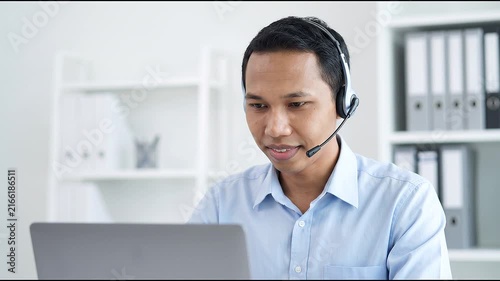 Indonesian business man speaking having virtual meeting on laptop. Wearing headset talking consulting on video call at home office call center.