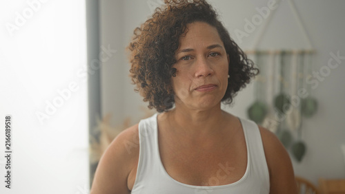 Fotografie Woman wearing white tanktop with bare shoulder closes eyes and presses lips in building; quiet resignation