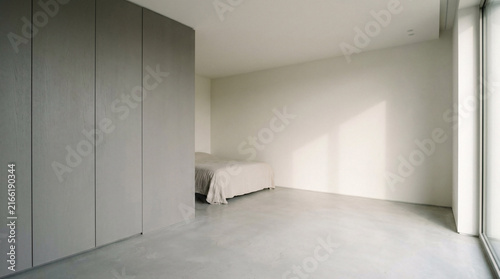 Minimalist modern bedroom with textured grey partition wall, simple bed, and natural light streaming through large window, calm and serene interior design concept