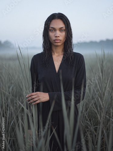 Woman in dark robe standing in misty marsh grass