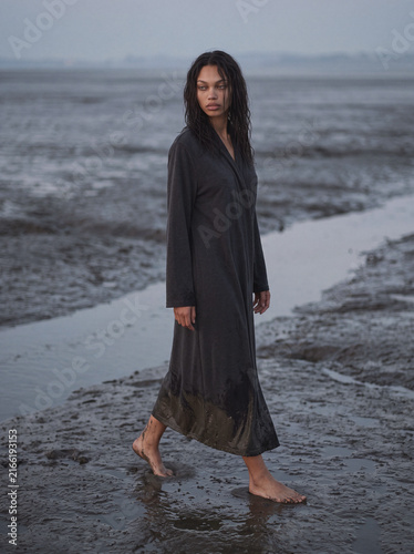 Woman walking barefoot across muddy tidal flats in dark robe