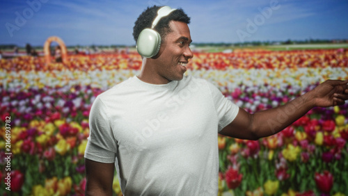 Obraz na płótnie Man wearing headphones pointing finger and smiling in studio before a tulip field backdrop, wearing a plain white tshirt; joyful calm