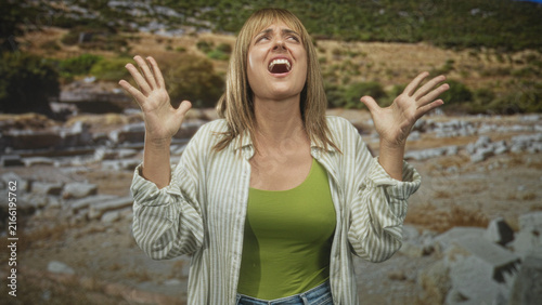 фотографія Woman with hands raised and open mouth, palms visible while screaming at stone ruins; anguish surrender