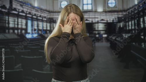 Fotografie Woman covers her face with hands while smiling in a museum gallery with display cases and rows of chairs; shy amusement