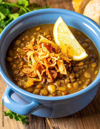 Hearty lentil soup garnished with a lemon wedge and fried onion bits is served in a blue ceramic bowl.