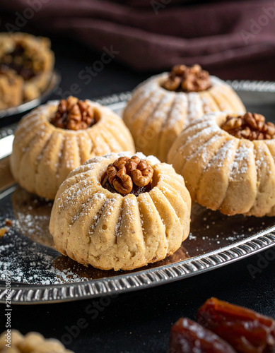 Maamoul cookies stuffed with dates and walnuts with decorative patterns on a silver platter with sugar dusting.