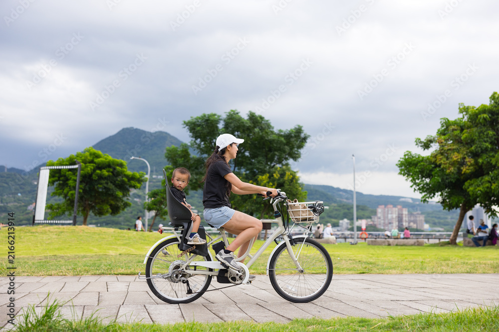 Fototapeta premium Mother riding bicycle with child near park