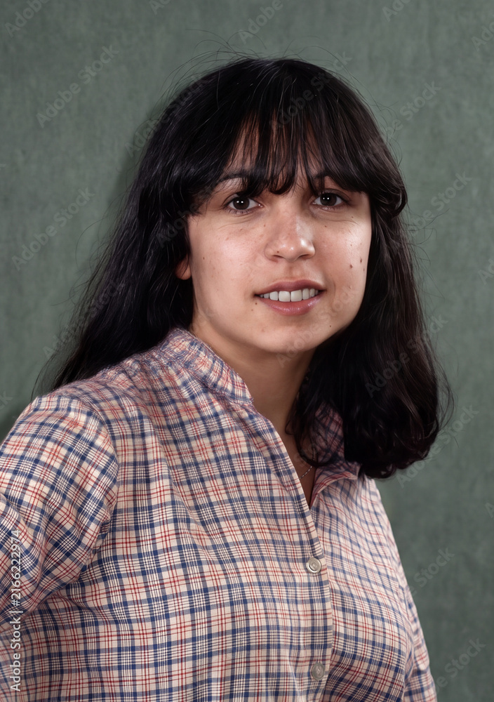 Obraz premium Portrait of a smiling young brunette woman in a plaid shirt against a green background.