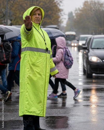 Woman traffic marshal directing pedestrians and cars on a rainy city street. Safety control and urban transportation concept with copy space.