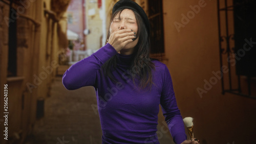 фотографія Woman painter covers mouth with hand while holding brush on a narrow cobblestone street, beret tilted, eyes closed; weariness solitude