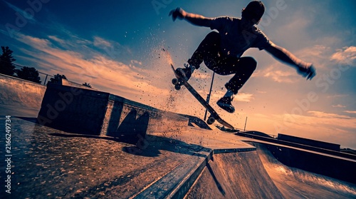 Plakat Skateboarder mid-air performing trick over concrete park ramps in dramatic setting
