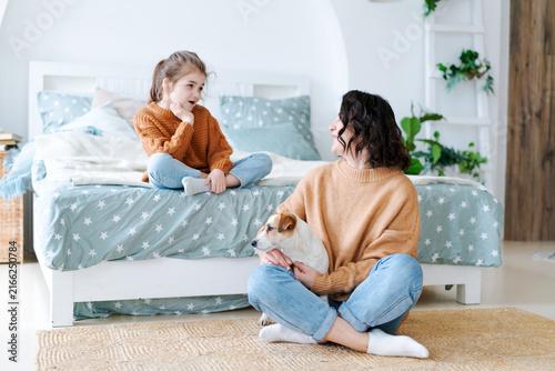 Fotografie Cheerful little caucasian girl in an orange sweater talking to her young mother
