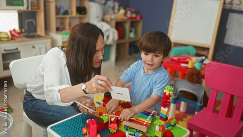 Woman shows flashcard while little boy holds mallets and plays xylophone and building blocks in a preschool building; playful learning.