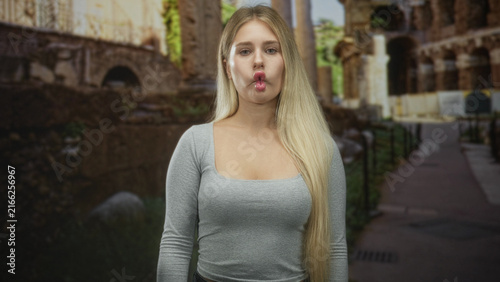 Fotografie Woman pouts in a fish face showing lips and long hair at ancient building pathway; youthful playful confidence