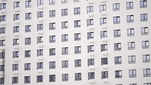 Modern white building exterior with grid pattern of windows wall-mounted air conditioners. Minimalist architectural detail under bright daylight. Neutral tones clean lines